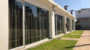 Un edificio moderno con amplios ventanales correderos, un camino de piedra y una pequeña zona ajardinada.