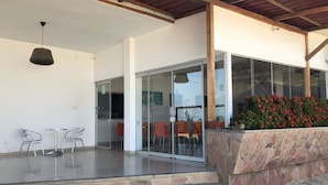 Un patio moderno al aire libre con puertas de cristal, una pared de piedra con flores rojas y un techo de madera.