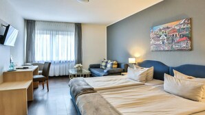 A hotel room with two beds, a desk, a chair, a sofa, and a painting on the wall. - Hotel Kolpinghaus Lingen (Lingen)