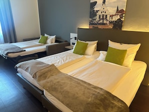 A hotel room with two beds, a nightstand, and a wall-mounted lamp. - Stadthotel im Kolpinghaus Lingen (Lingen)