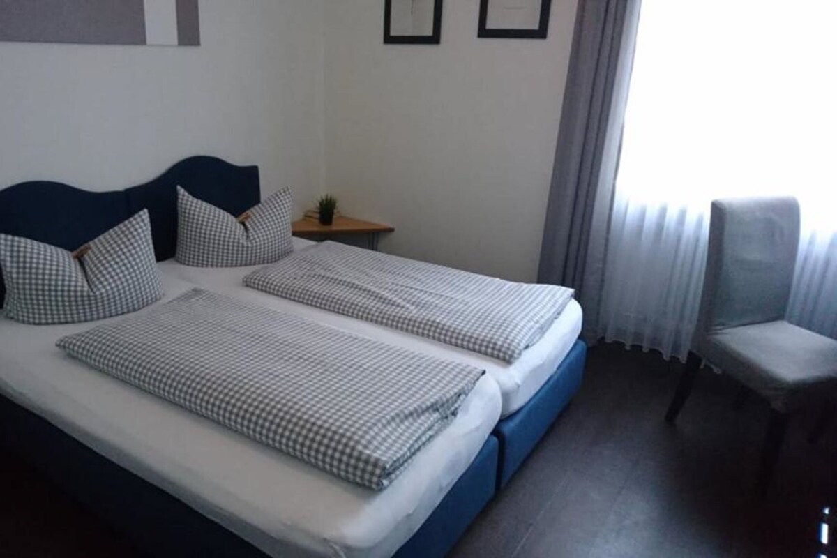 A double bed with checkered bedding, a bedside table with a lamp, and a chair.