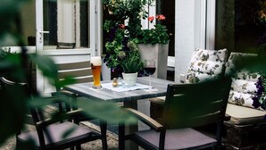 An outdoor seating area with a table, chairs, a glass of beer, and a potted plant. - Hotel Kolpinghaus Lingen (Lingen)