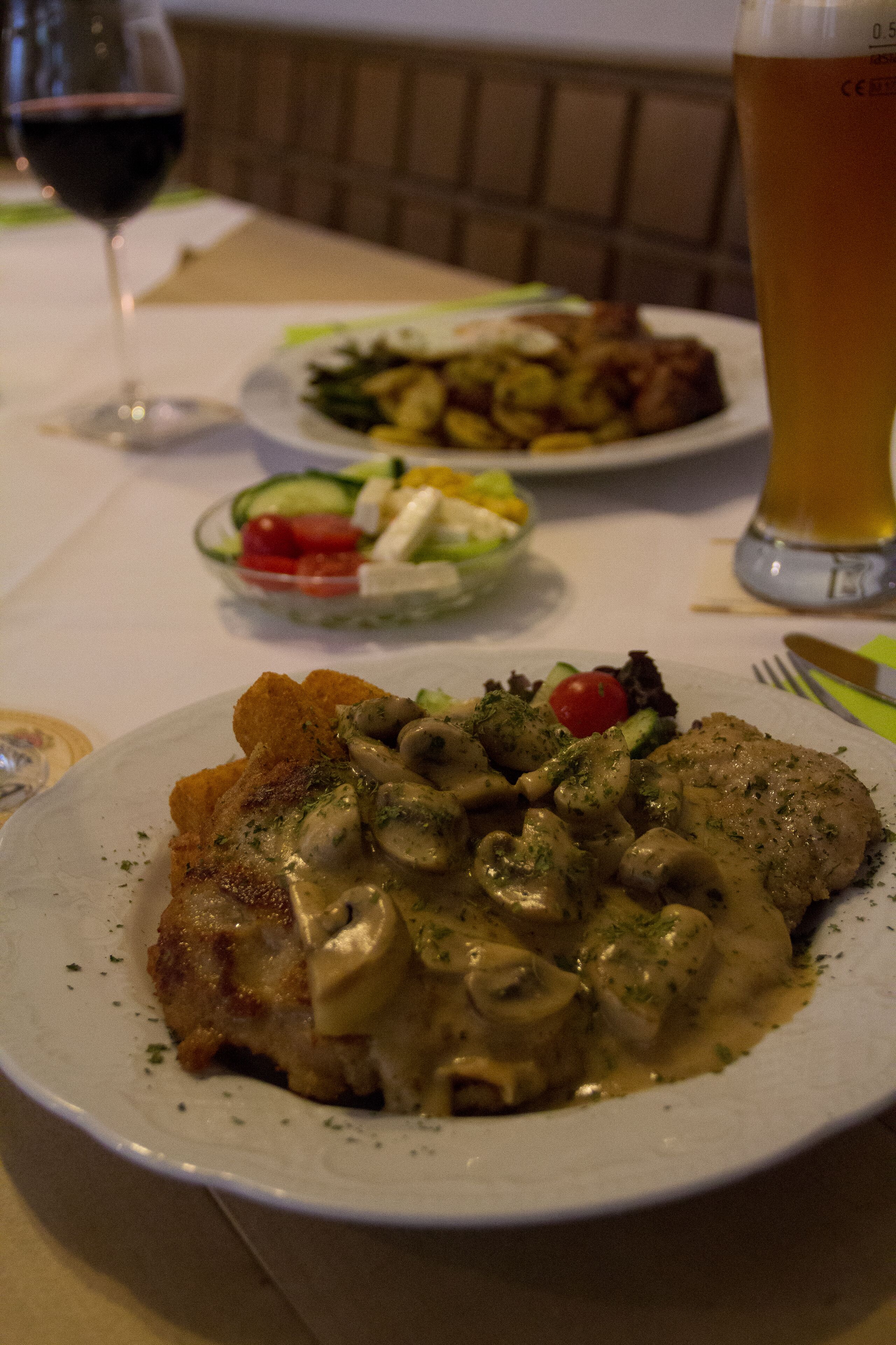 A dining table with plates of food, a glass of beer, and a wine glass.