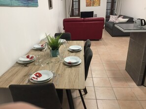 A dining area with a wooden table set for four, surrounded by chairs. A red sofa and a grey couch are visible in the background. - MARSEILLE ST CHARLES / PORTE D ’IX (Marseille)