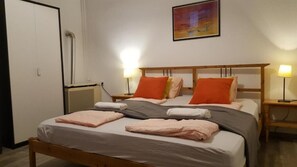 Una habitación de hotel con una cama, dos lámparas de noche, un cuadro en la pared y una puerta.
