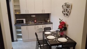 Una cocina compacta con armarios blancos, un microondas y un comedor con mesa, sillas y un jarrón de flores.