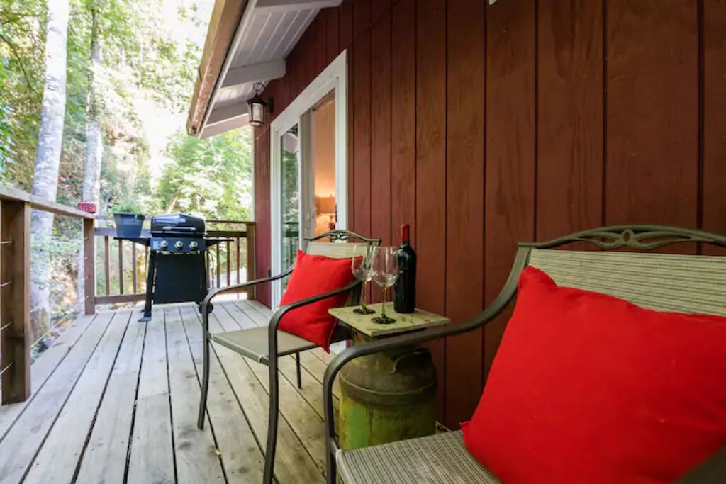 Une terrasse en bois avec une chaise en métal et une table, un barbecue et une poubelle.