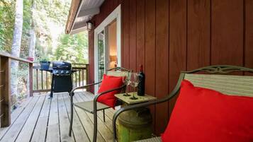Une terrasse en bois avec une chaise en métal et une table, un barbecue et une poubelle.
