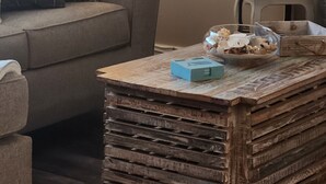 Una sala de estar con un sofá, una mesa de centro con objetos decorativos, una lámpara y un jarrón con plantas secas.