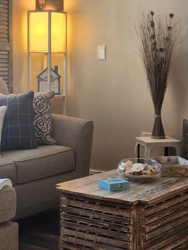 Una sala de estar con un sofá, una mesa de centro con objetos decorativos, una lámpara y un jarrón con plantas secas.