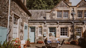 A stone building with a courtyard, a wooden bench, a table with chairs, and a street lamp. - Historic Arcadia: Heritage Coachman Lodge on 2000-acre Seaside Estate (Portpatrick)
