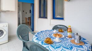 A dining area with a table set for two, a washing machine, and a window with blue shutters.