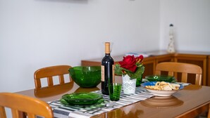A dining table with green glassware, a wine bottle, a rose, and a bowl of snacks.