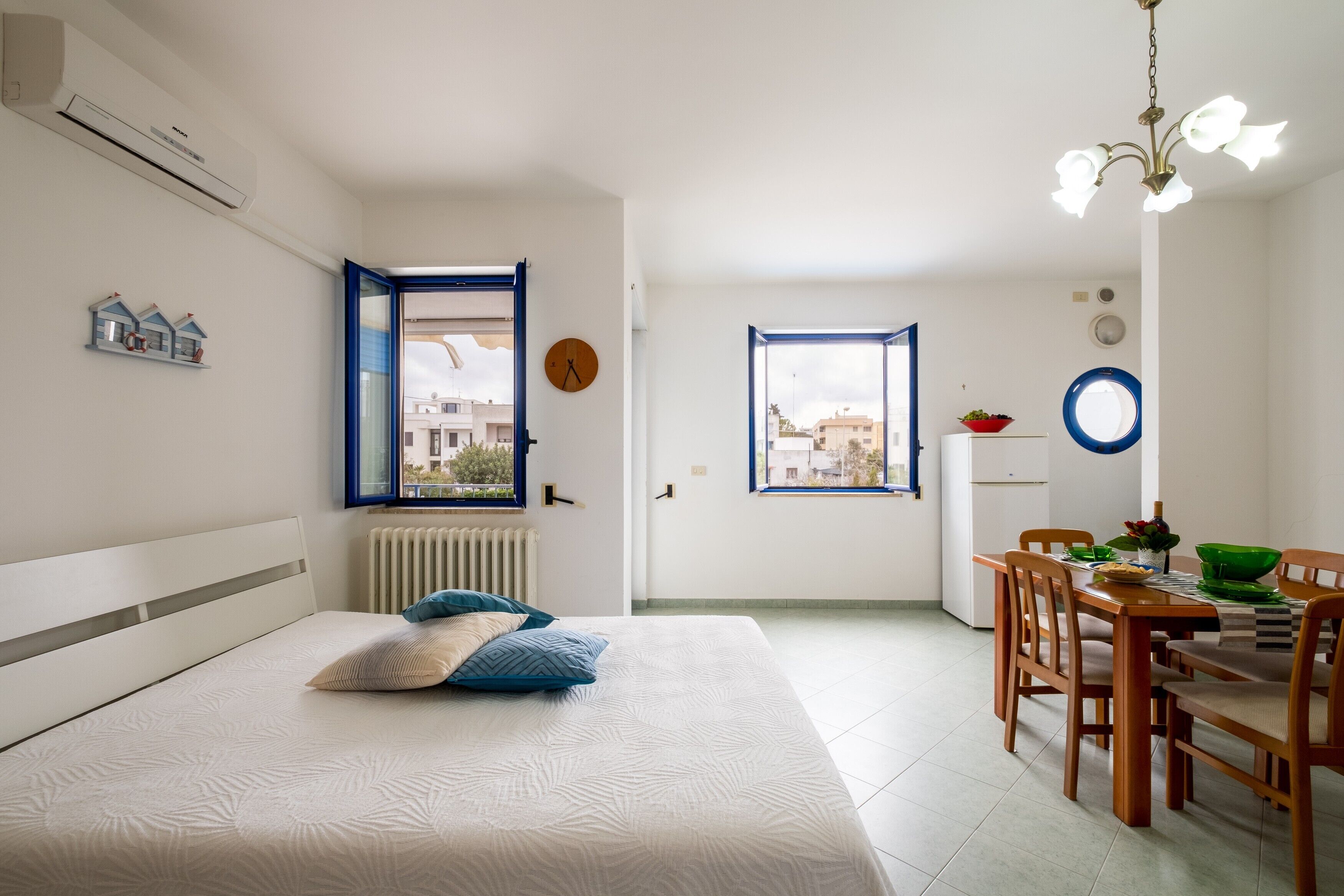 Una camera da letto con un letto, un'area pranzo con tavolo e sedie, una finestra e un termosifone.