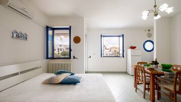 Una camera da letto con un letto, un'area pranzo con tavolo e sedie, una finestra e un termosifone.
