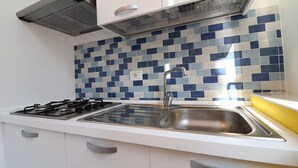 A kitchen with a gas stove, stainless steel sink, and a tiled backsplash. - Charming Holiday Apartment "Casa Vacanze Aura" with Air Conditioning (Otranto)