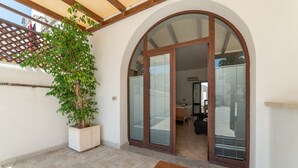 Un patio cubierto con una planta en maceta, un banco de madera y una puerta que da a un espacio interior.