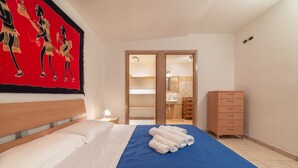Habitación de hotel con cama, cómoda de madera, baño visible a través de una puerta abierta y una obra de arte roja en la pared.