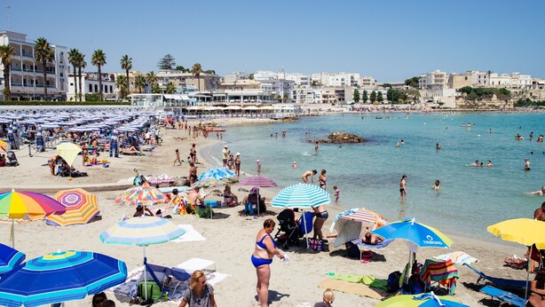 Una playa con sombrillas, gente y edificios al fondo.