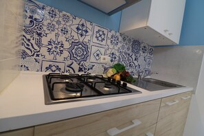 A kitchen with a gas stove, a sink, and a backsplash with blue and white tiles.