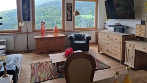 A cozy living room with a fireplace, a television, and large windows offering a forest view. - Apartment 'Baumannhof Hasental - Adults Only' with Mountain View, Shared Garden and Wi-Fi (Gfrill/Tisens bei Lana)