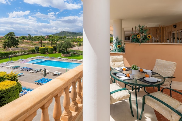 A balcony with a pool view, a dining area with a table and chairs, and a plant on the wall.