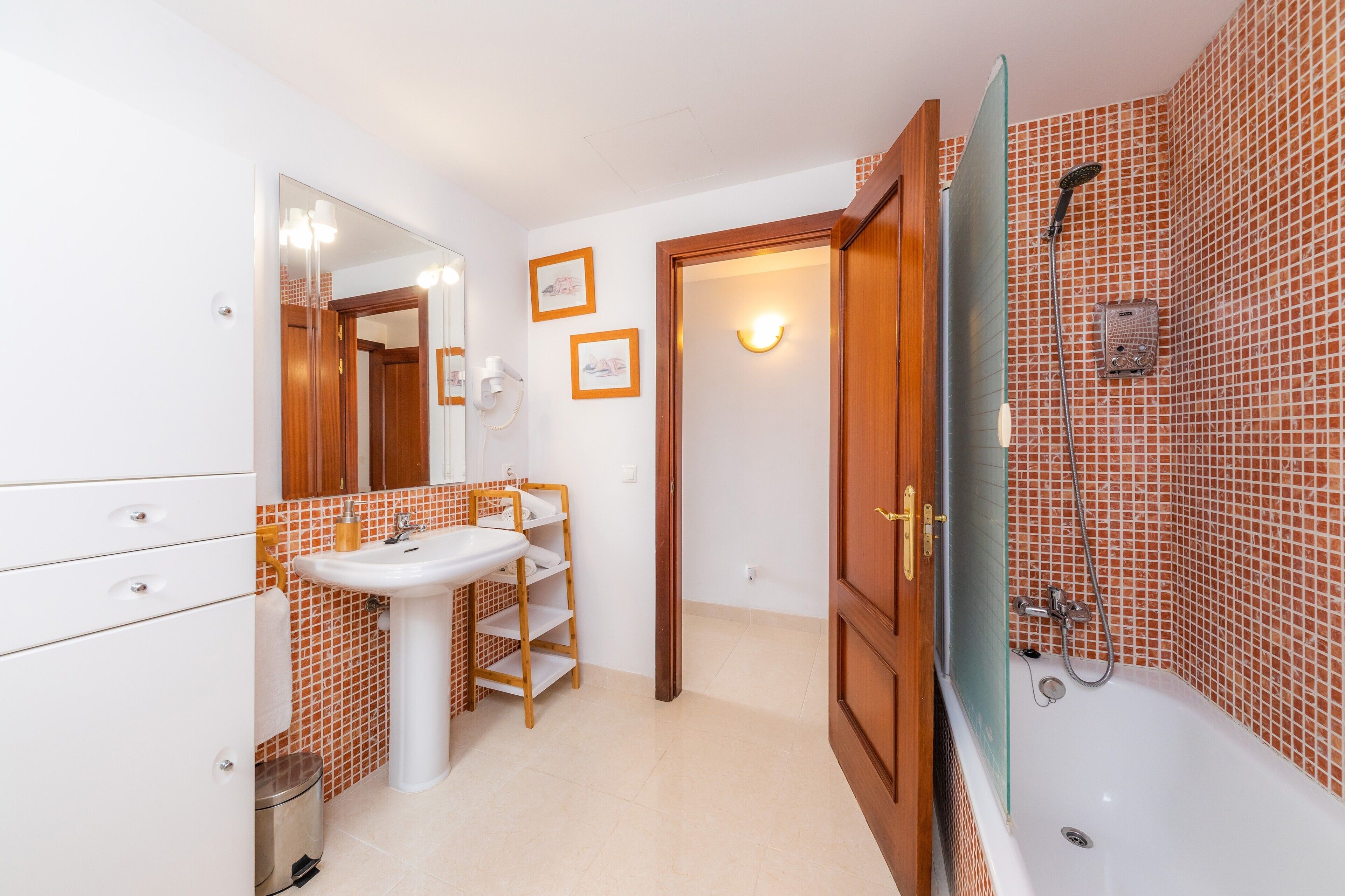 A bathroom with a sink, mirror, shower, and tiled walls.