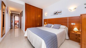 A hotel room with a large bed, wooden headboard, bedside lamps, a nightstand, and a wardrobe.