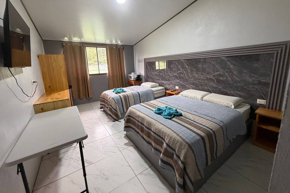 A hotel room with two beds, a desk, a TV, and a window with curtains.
