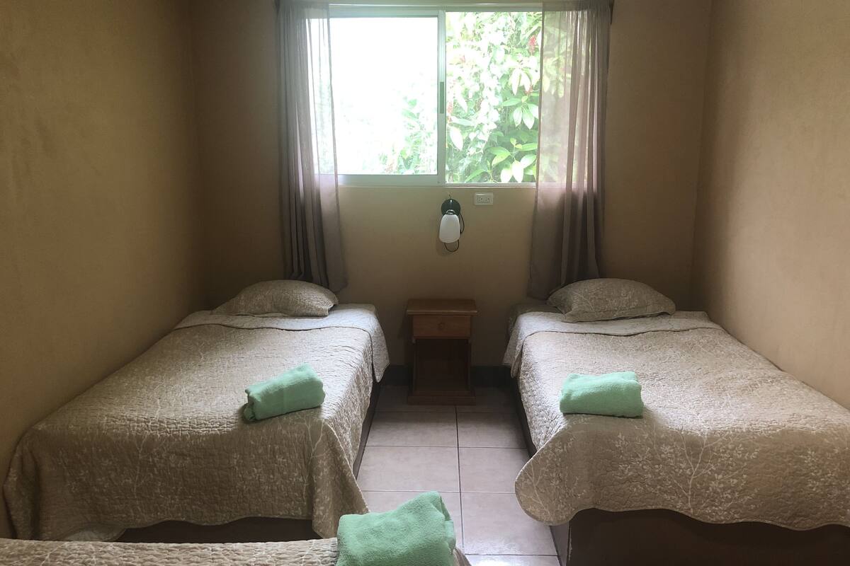 A room with two beds, each with a green towel, a nightstand, and a wall-mounted lamp.