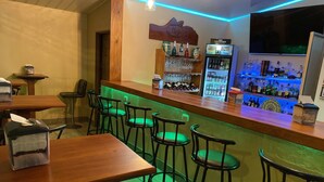 Una zona de bar con taburetes y una barra, un refrigerador lleno de bebidas y un televisor colgado en la pared.