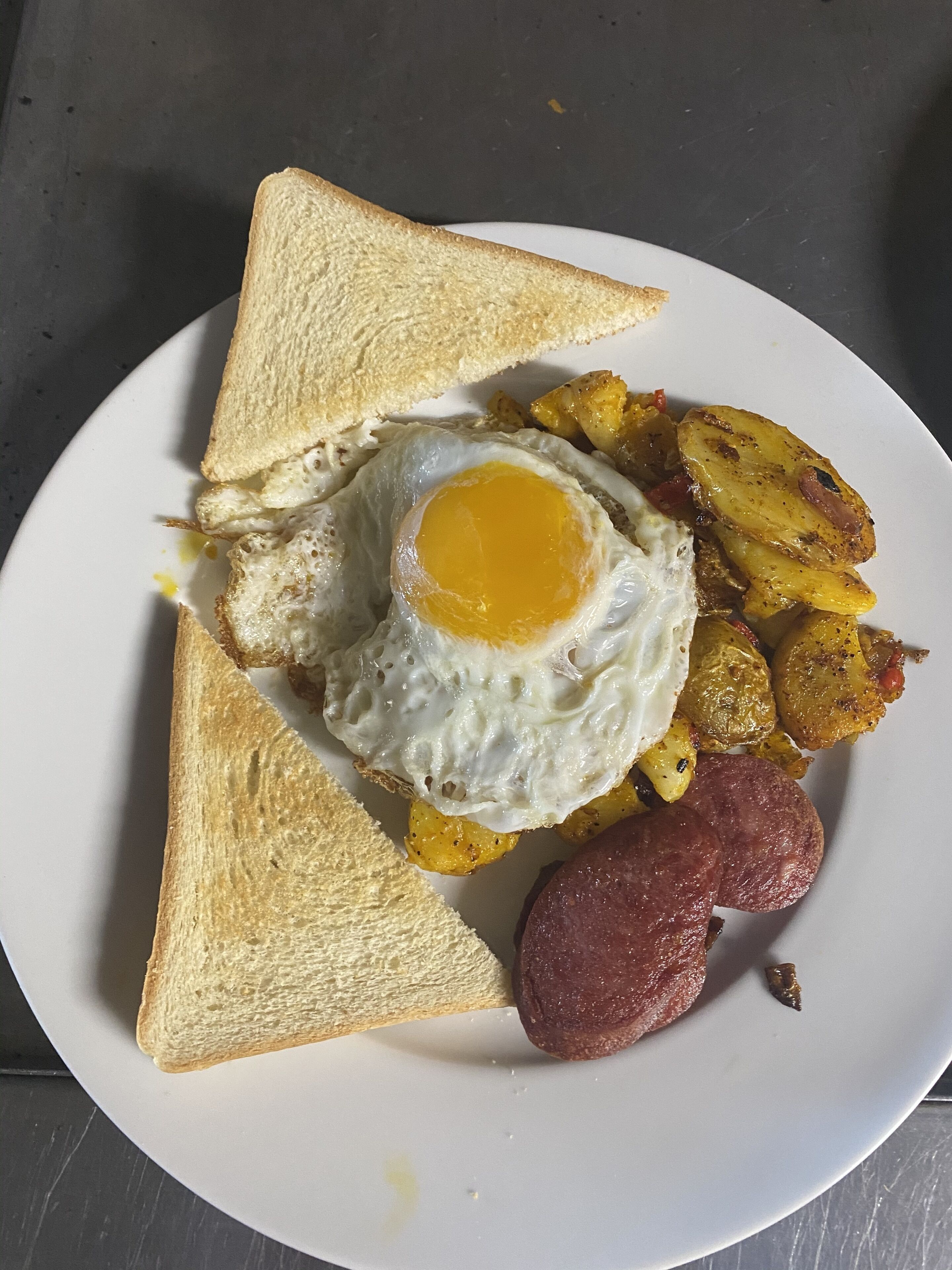 A plate with toast, a fried egg, roasted potatoes, and a sausage.