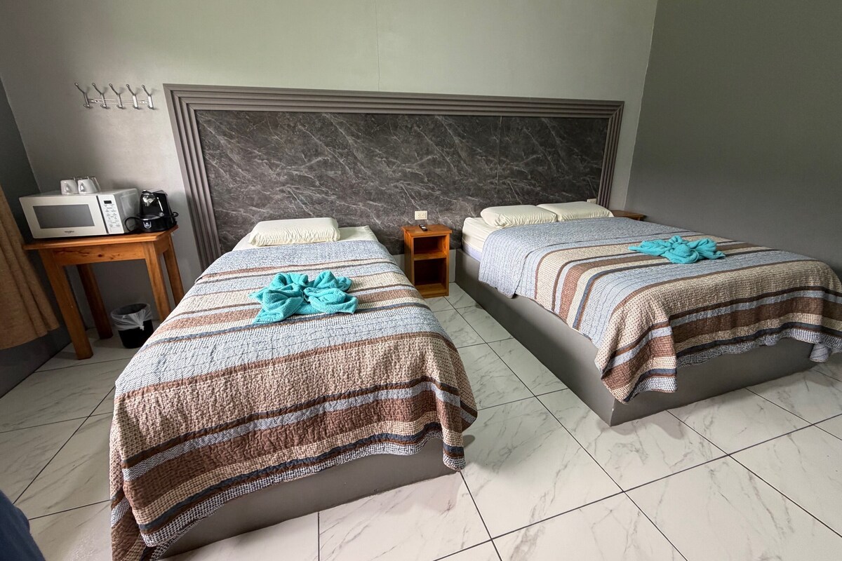 Habitación de hotel con dos camas, una mesita de noche de madera, un microondas y un cubo de basura.