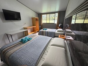 A hotel room with two beds, a TV, a wooden cabinet, a window with a view, and a small table with a remote control. - Hotel Uran (Rivas)