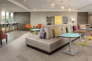 Um lobby moderno com sofá, cadeiras, mesas e uma área de cozinha.