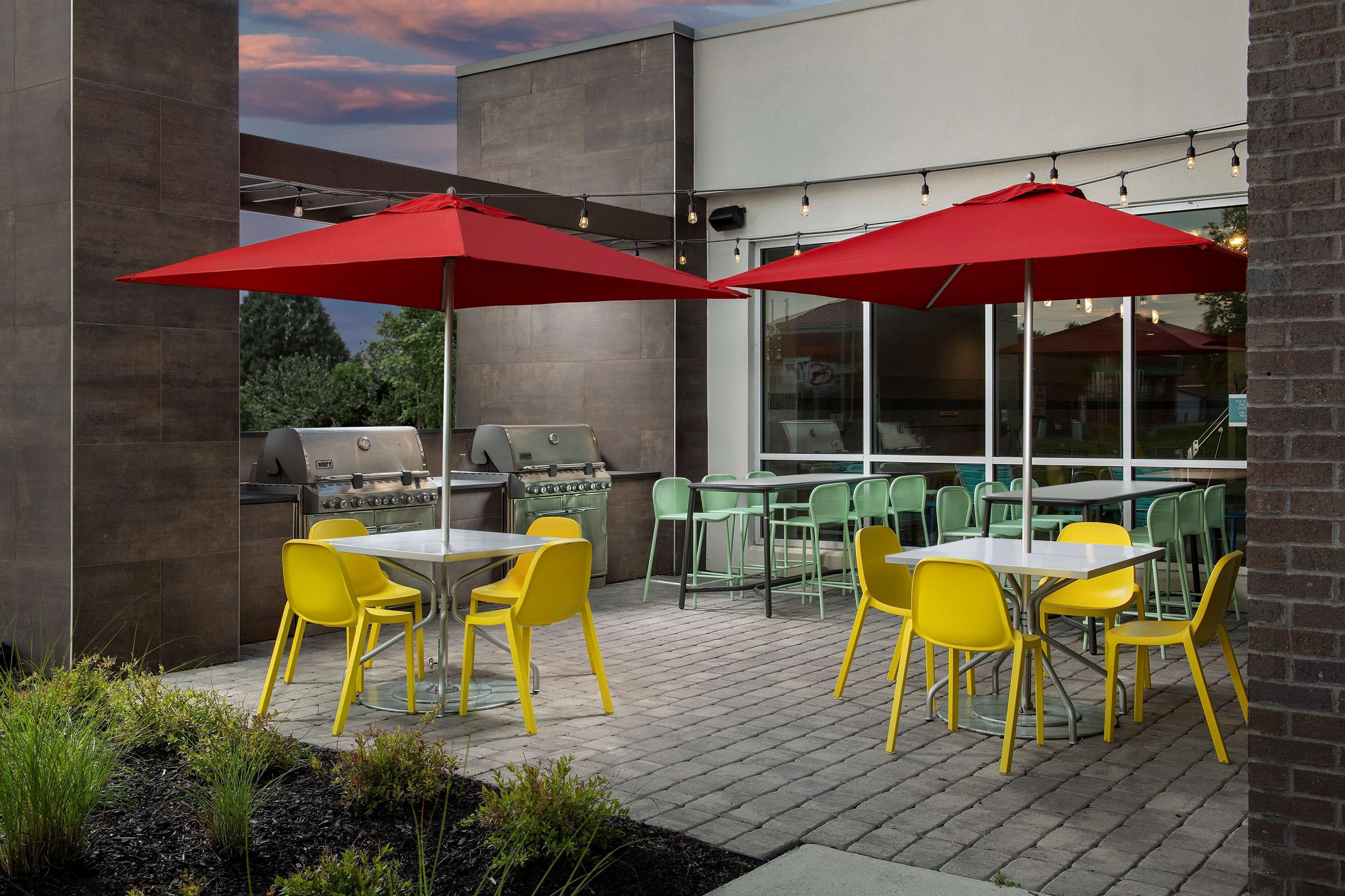 An outdoor patio with yellow chairs and red umbrellas, a grill, and a brick wall.