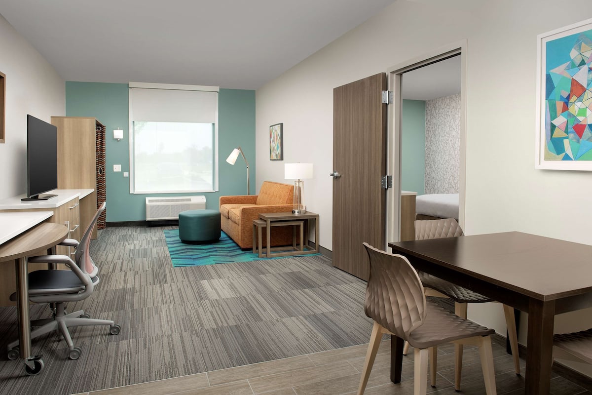 Moderni hotellihuone, jossa on työpöytä, toimistotuoli, sohva ja ruokapöytä.