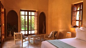 A spacious room with a large bed, two wicker chairs, a small table, and a window with a view of greenery. - Domaine Casa Cecilia (Oulad Hassoune)