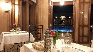 A dining area with tables set for two, featuring white tablecloths, silverware, and glassware. There are decorative vases with flowers and a water bottle on the tables. - Domaine Casa Cecilia (Oulad Hassoune)