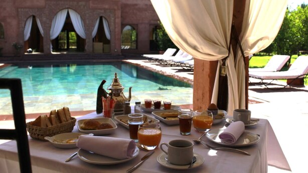 A table set for breakfast with a pool view, including plates, cups, and a teapot. - Domaine Casa Cecilia (Oulad Hassoune)