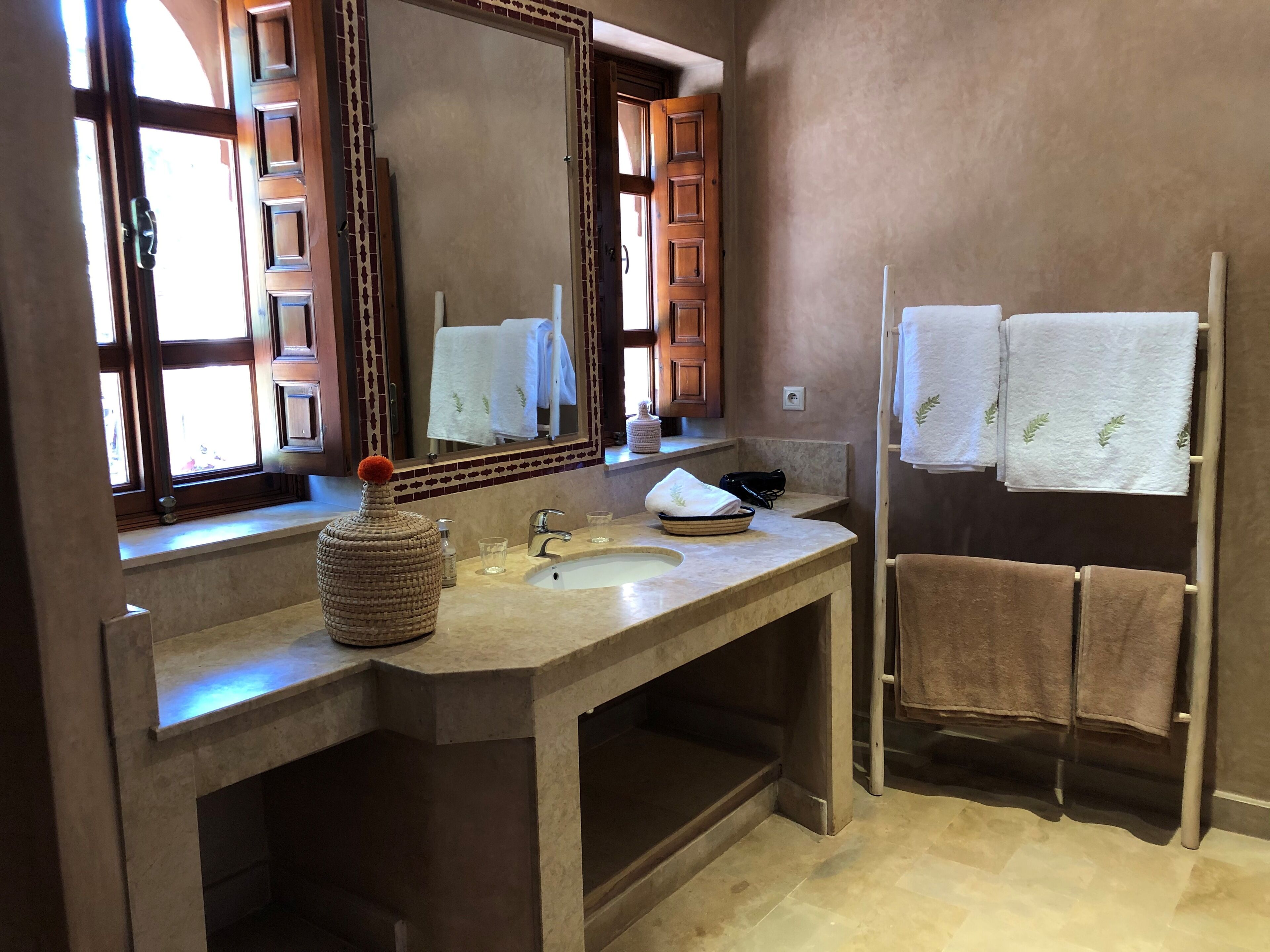 A bathroom with a large mirror, a sink, a towel rack with towels, and a decorative vase.