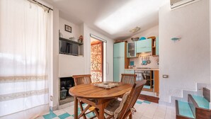 A dining area with a wooden table and chairs, a kitchen with teal cabinets, and a staircase with blue steps.