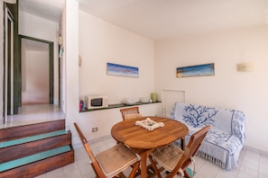 A dining area with a round wooden table, four chairs, a sofa, and two wall-mounted paintings.