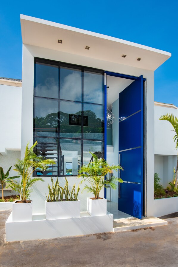 A modern building with a glass facade, white exterior walls, and a blue door. There are potted plants in front.
