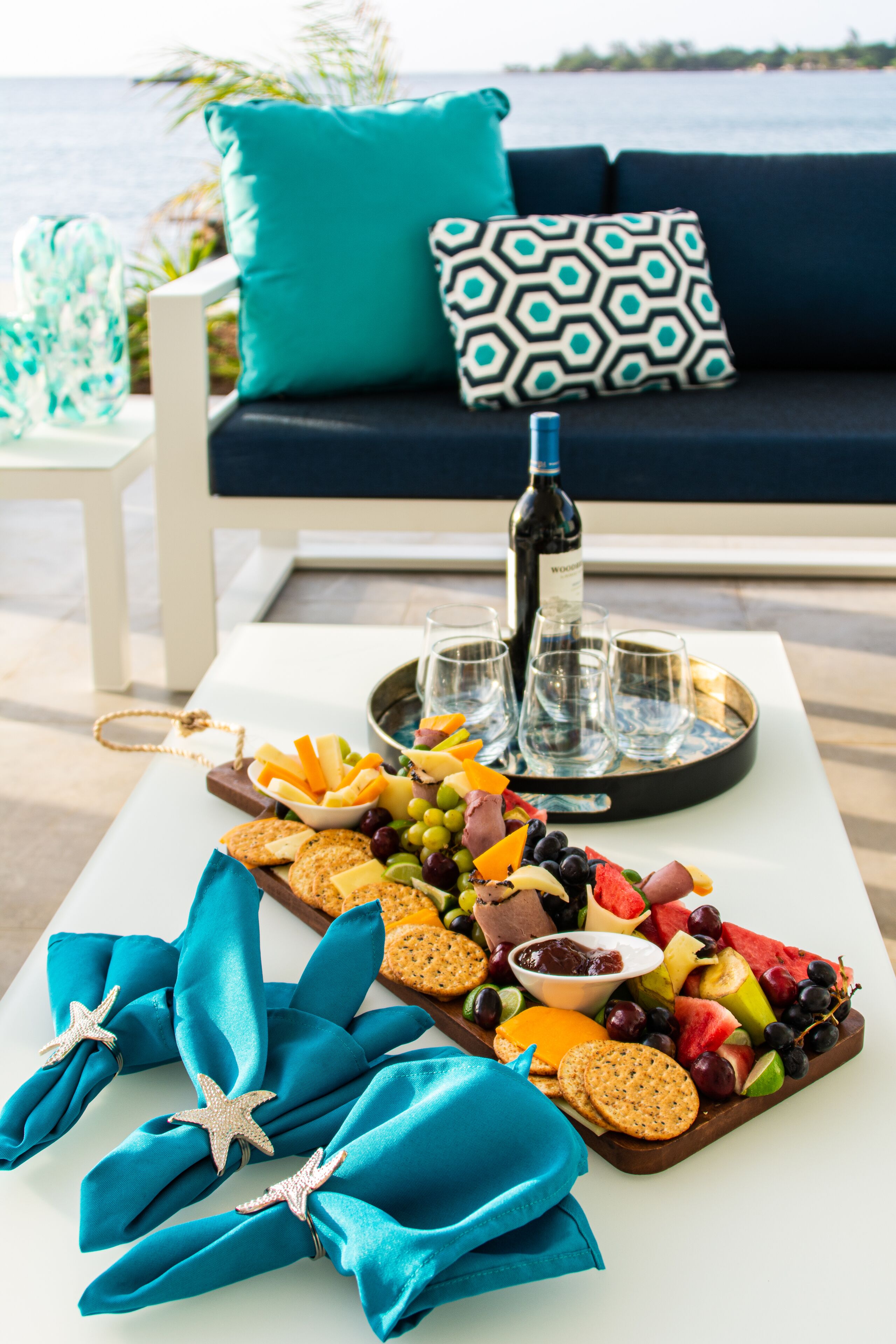 A table with a charcuterie board, wine bottle, glasses, and a tray with snacks and fruits.
