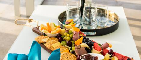 A table with a charcuterie board, wine bottle, glasses, and a tray with snacks and fruits.