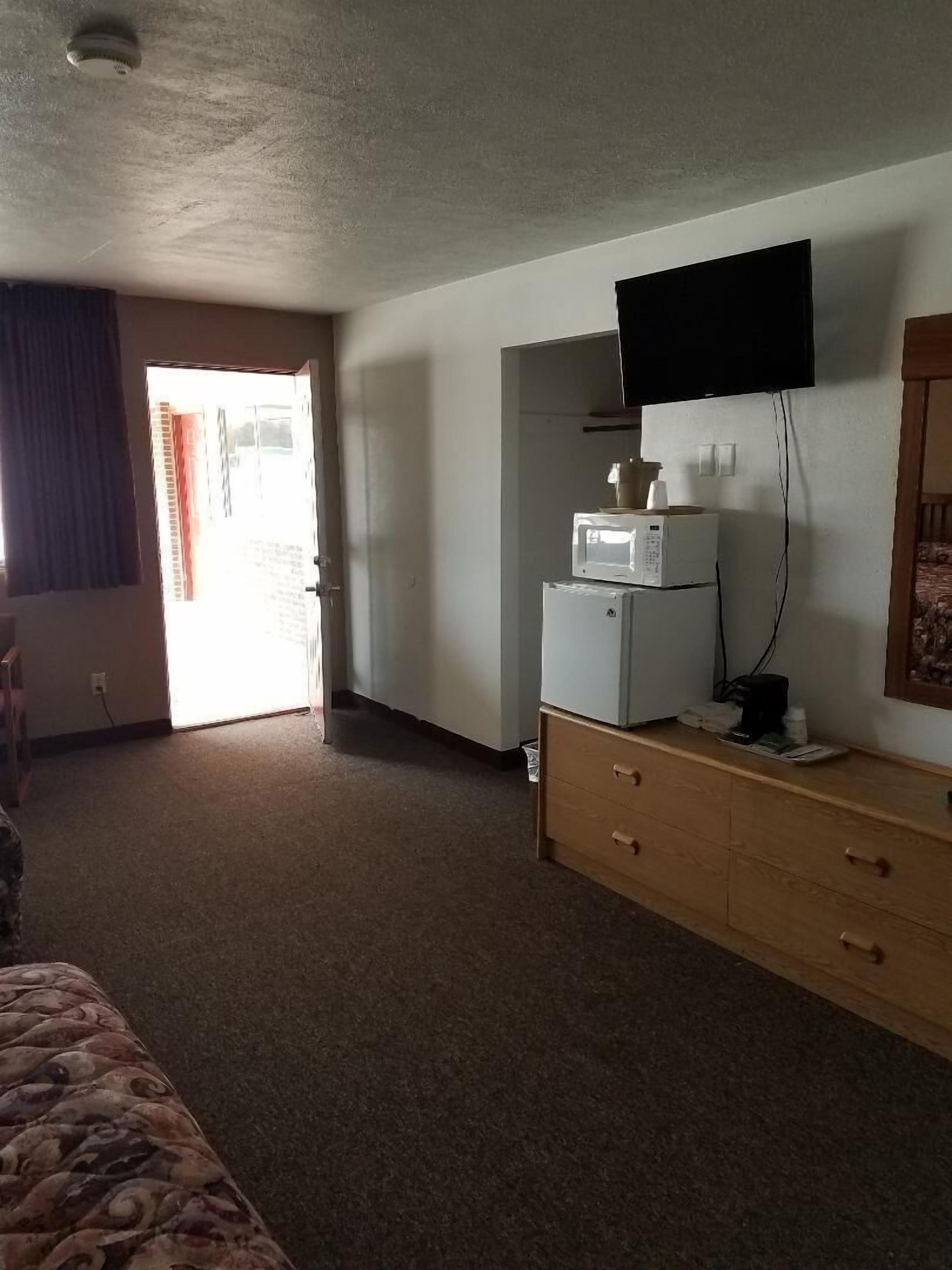 A hotel room with a bed, a dresser, a microwave, a television, and a door leading to a balcony.