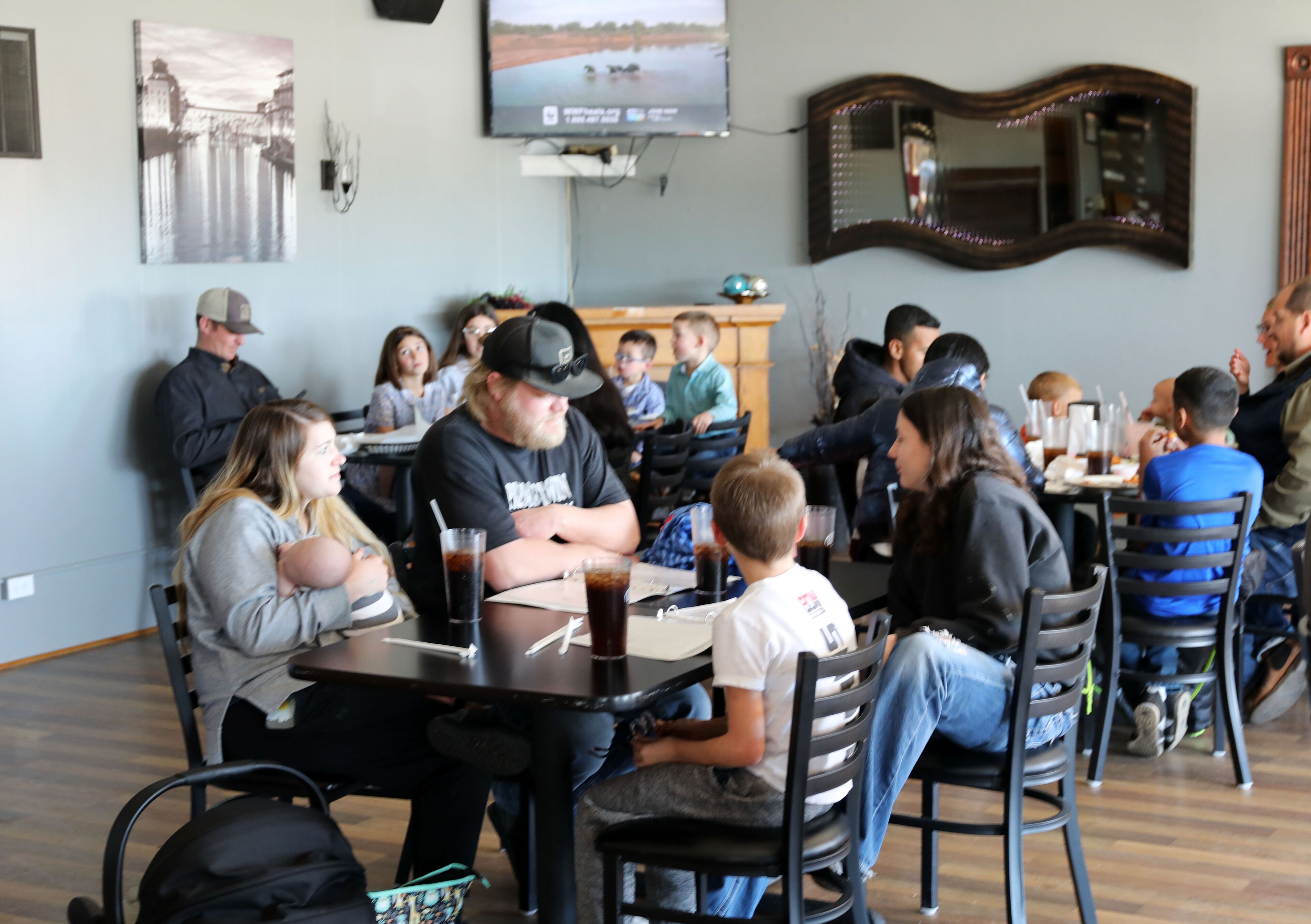 A restaurant with tables and chairs, a television mounted on the wall, and a mirror above the counter.