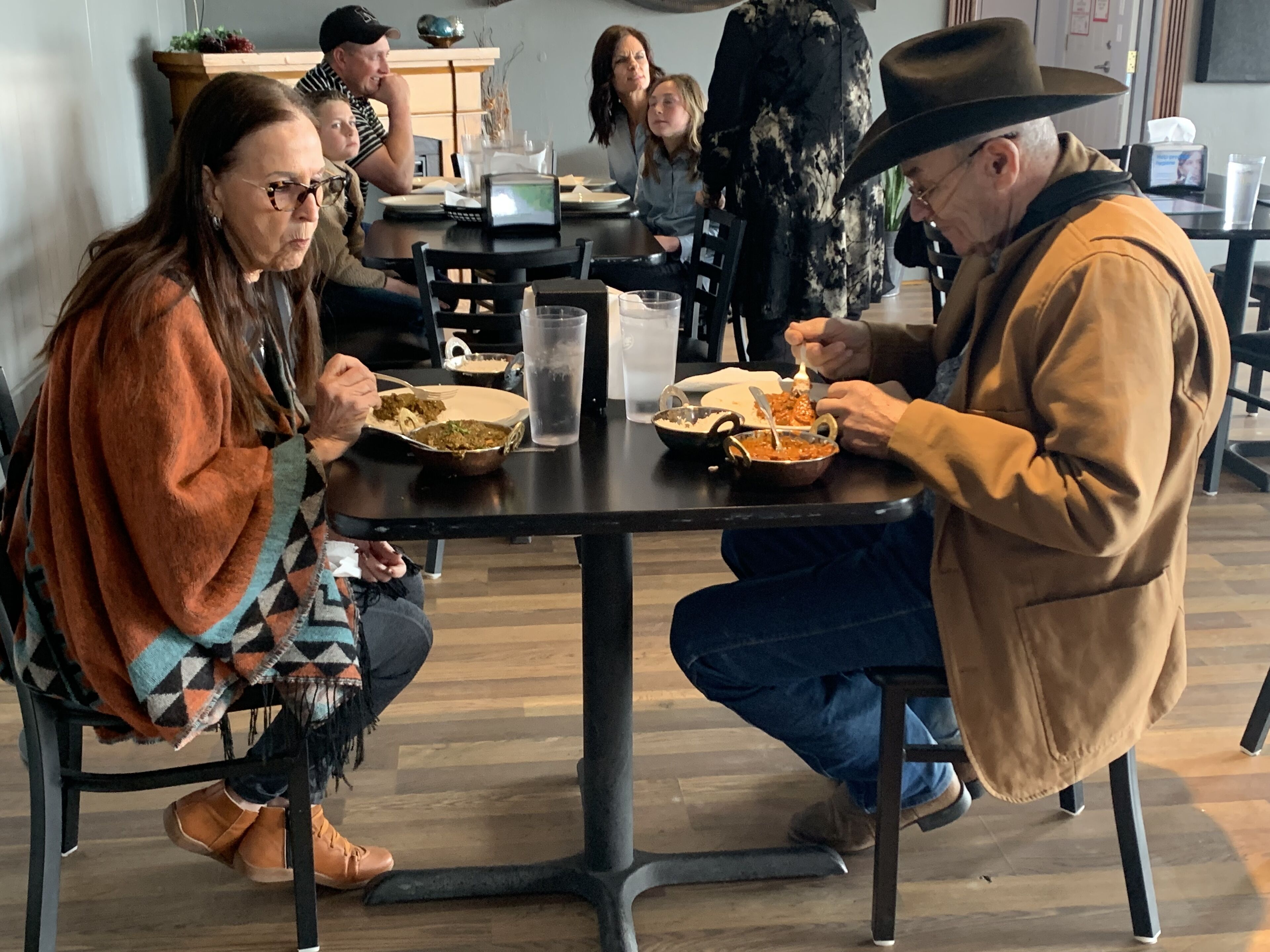 Una mesa de comedor con personas sentadas alrededor, comiendo.