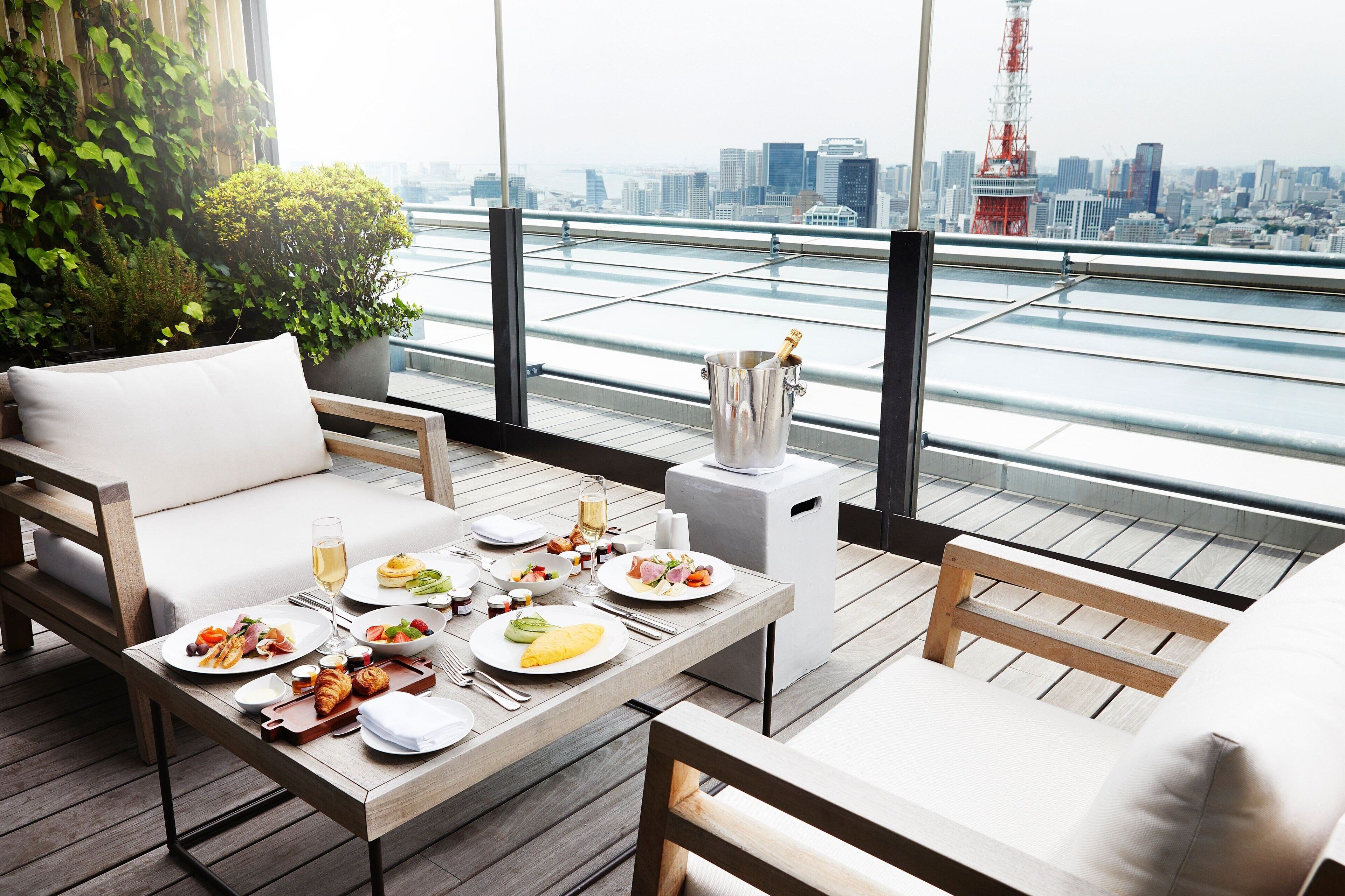 A rooftop dining area with a table set for a meal, a champagne bottle, and a city view.